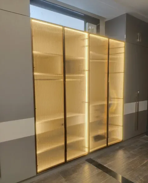 Full-height display cabinet with slim brass-toned profile frames and fluted glass panels, lit from inside, in a completed Ikka Kitchen installation